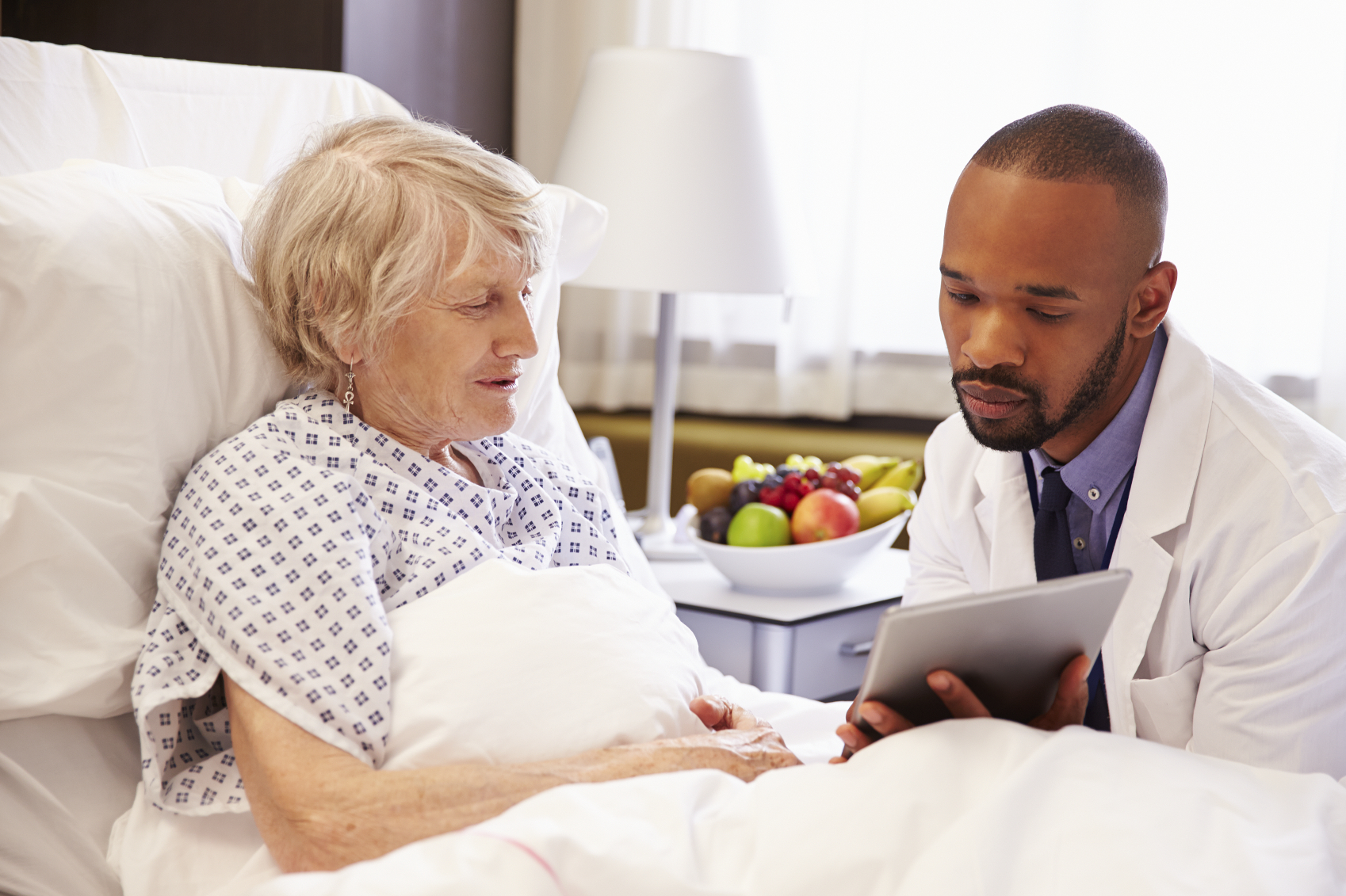 Doctor Talking To Senior Female Patient In Hospital Bed